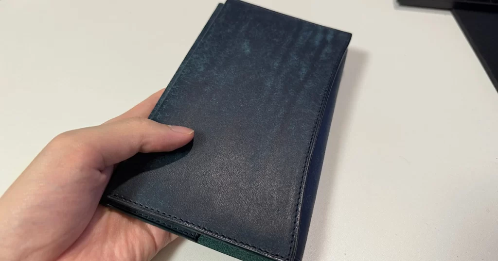 手に持った UNROOF のプエブロレザー製本革ブックカバー（新書サイズ／ナジョナーレ藍）の表面を写した写真